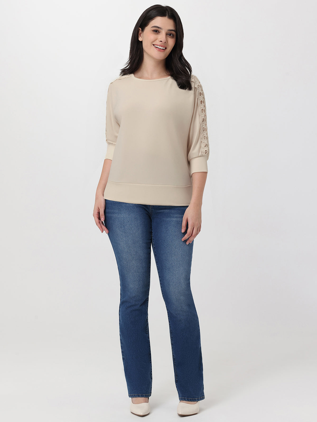 Woman wearing a beige sweater with lace sleeves and blue jeans on a white background