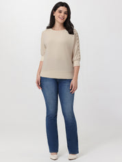Woman wearing a beige sweater with lace sleeves and blue jeans on a white background