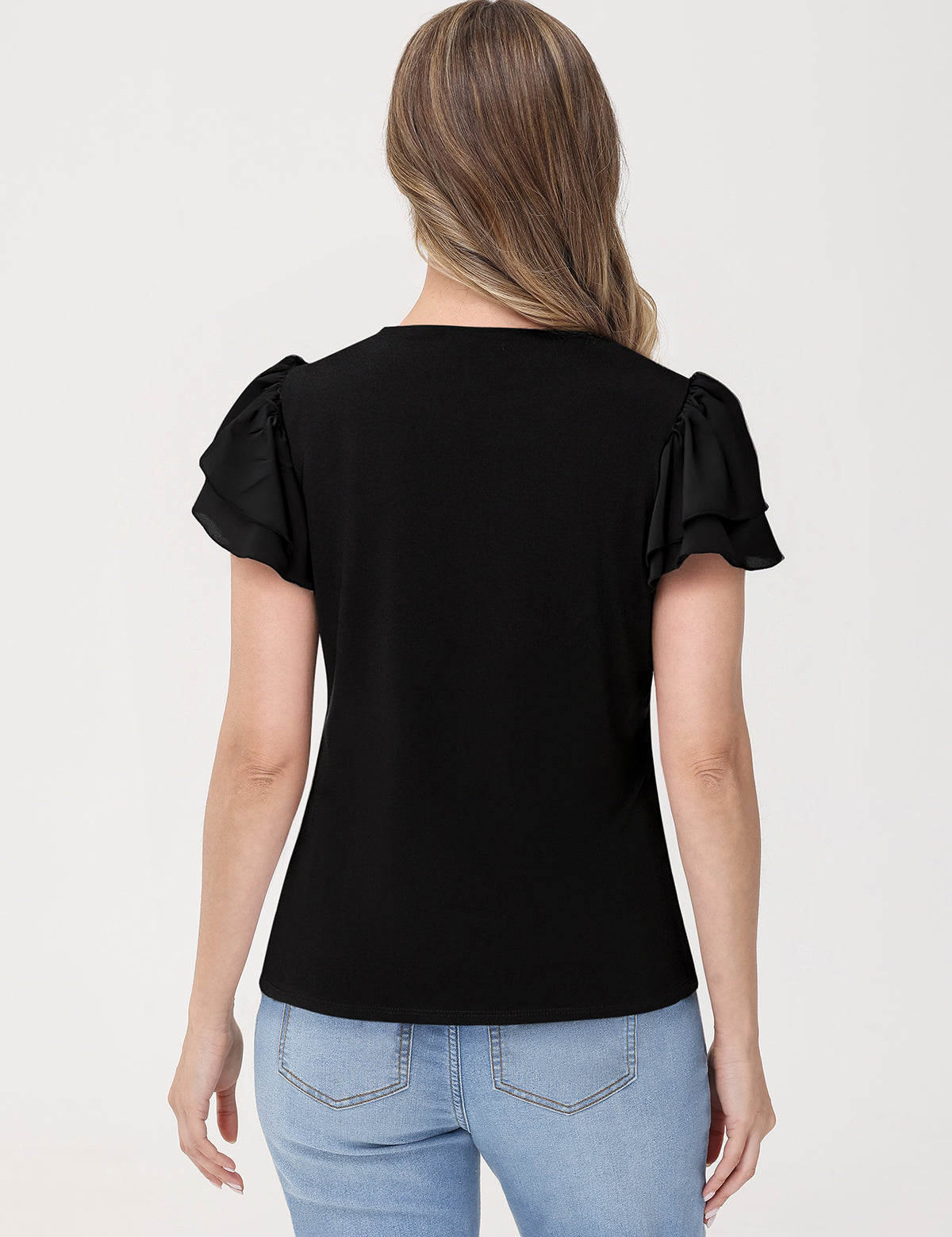 Woman wearing a black top with ruffled sleeves and light blue jeans on a white background