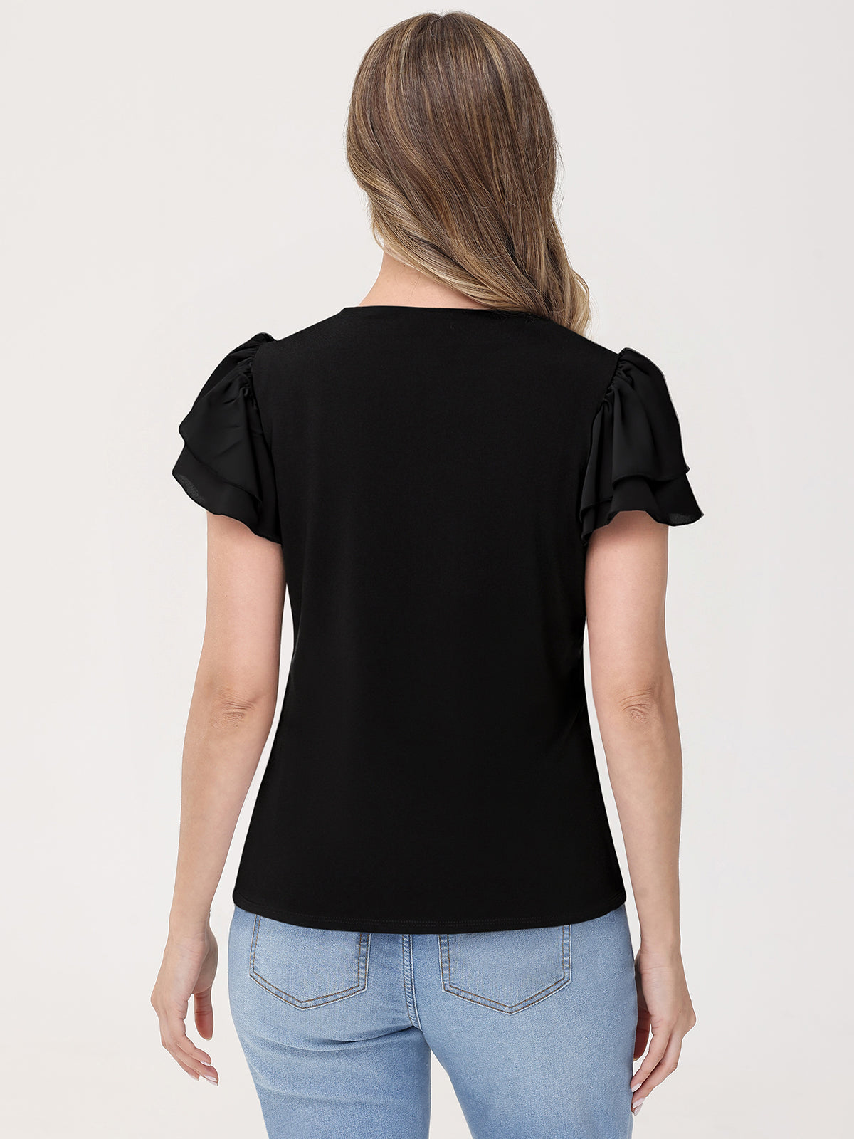Woman wearing a black top with ruffled sleeves and light blue jeans on a white background
