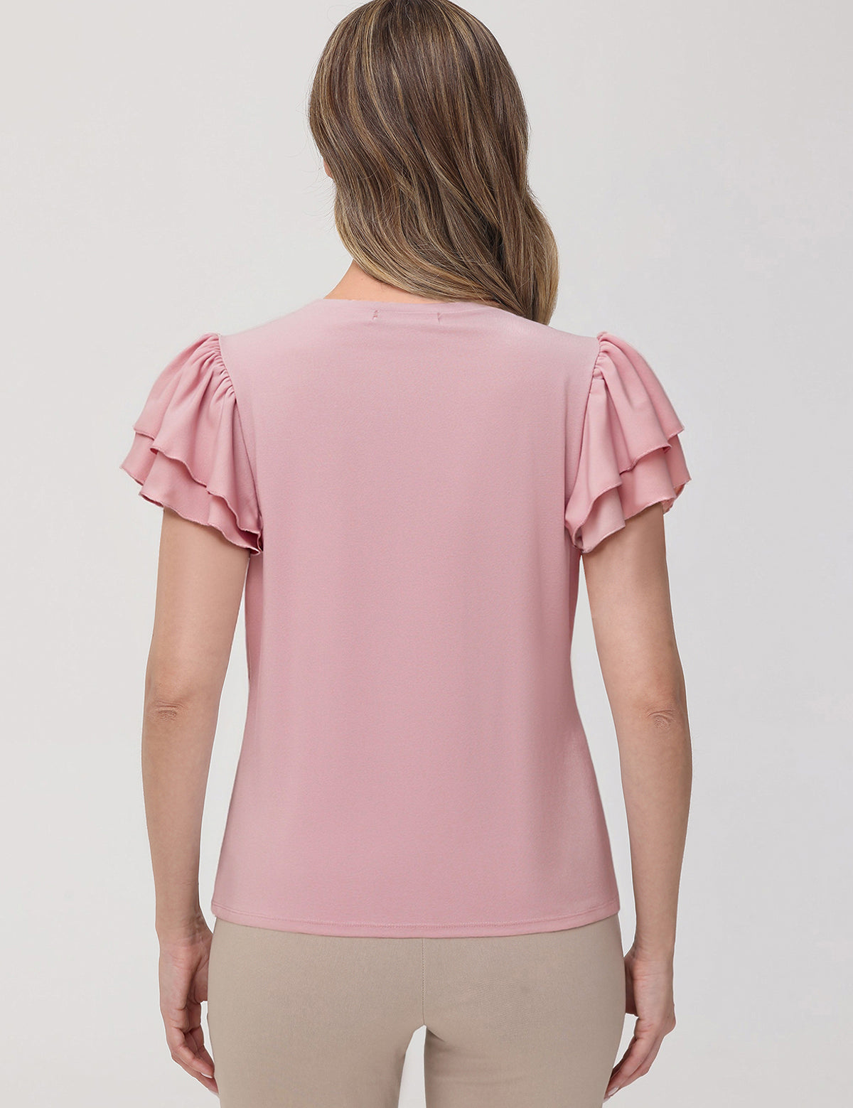 Woman wearing a pink blouse with ruffled sleeves on a plain background