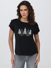 Woman wearing a black t-shirt with tree designs on a plain background