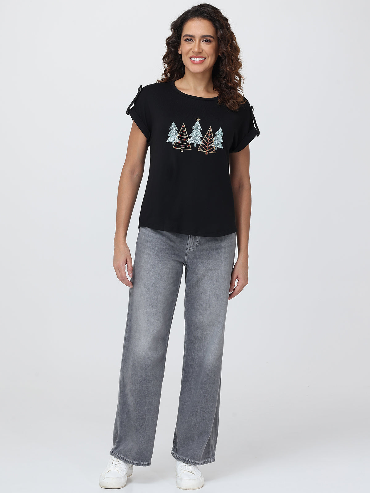 Woman wearing a black t-shirt with tree design and gray jeans on a white background