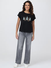 Woman wearing a black t-shirt with tree design and gray jeans on a white background