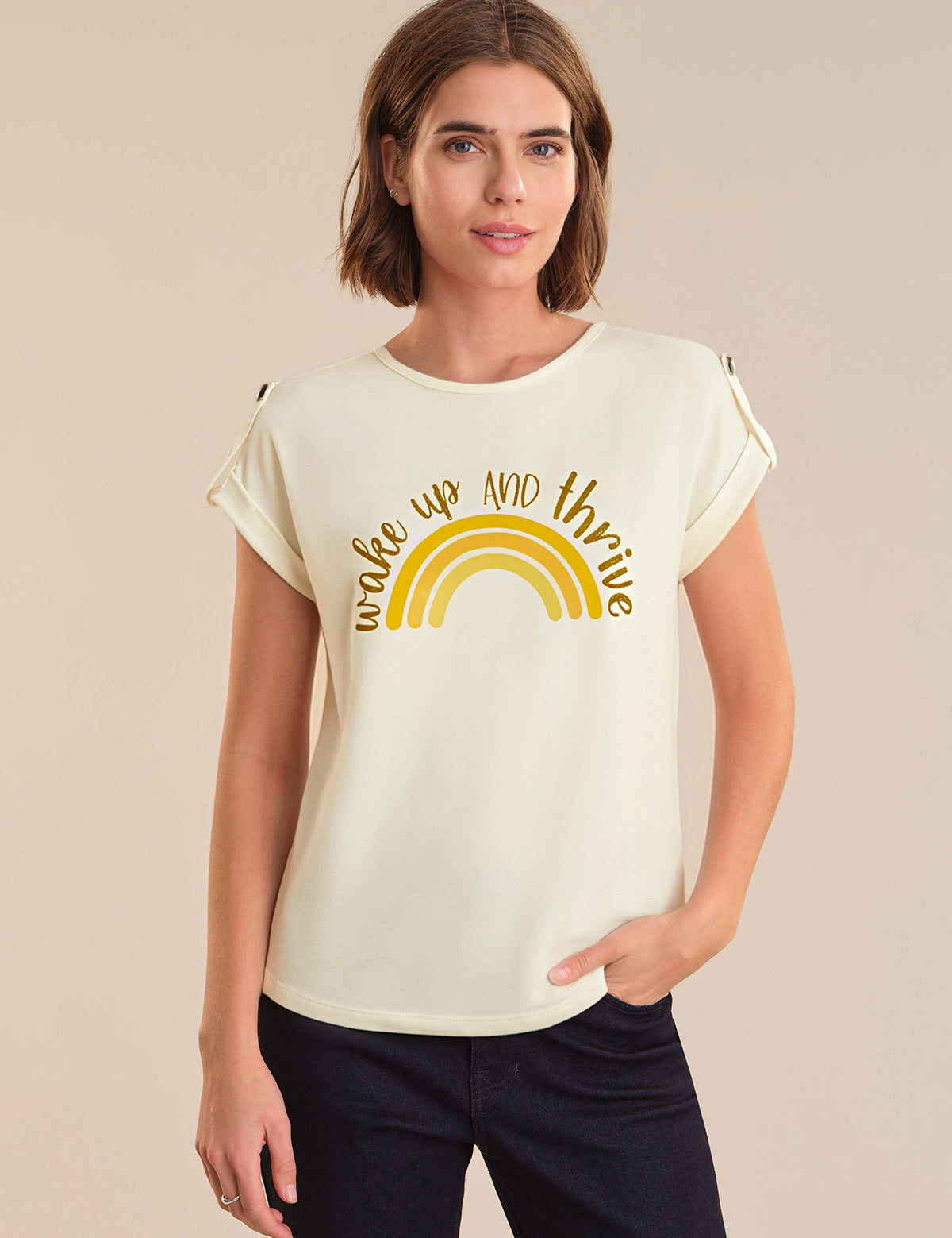 Woman wearing a cream t-shirt with a yellow rainbow and text design on a beige background
