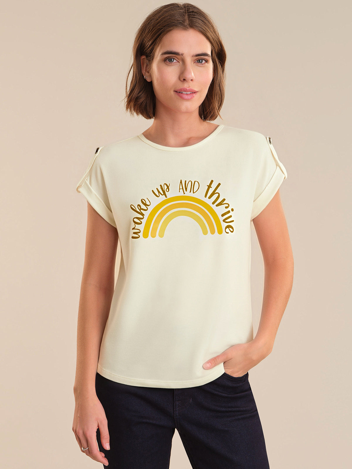 Woman wearing a cream t-shirt with a yellow rainbow and text design on a beige background