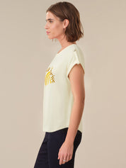Woman wearing a light-colored t-shirt with a yellow graphic design on a beige background
