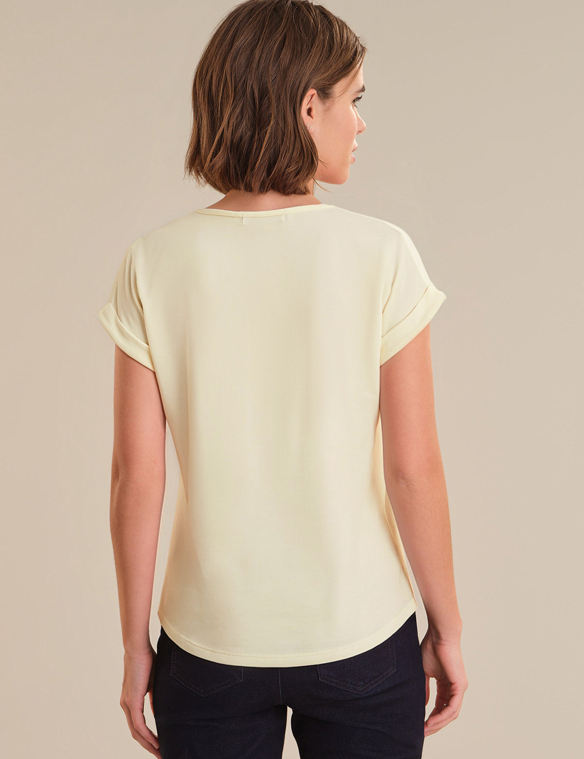 Woman wearing a light yellow top and dark pants on a beige background