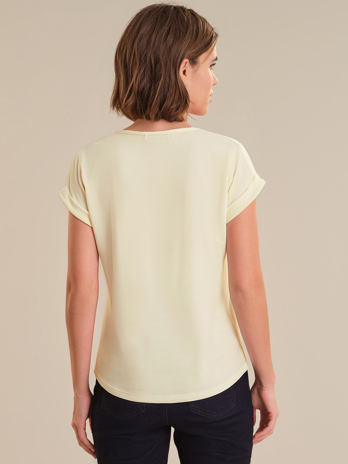 Woman wearing a light yellow top and dark pants on a beige background