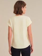 Woman wearing a light yellow top and dark pants on a beige background