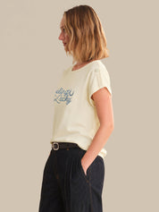 Woman wearing a light-colored t-shirt with text, standing against a plain background
