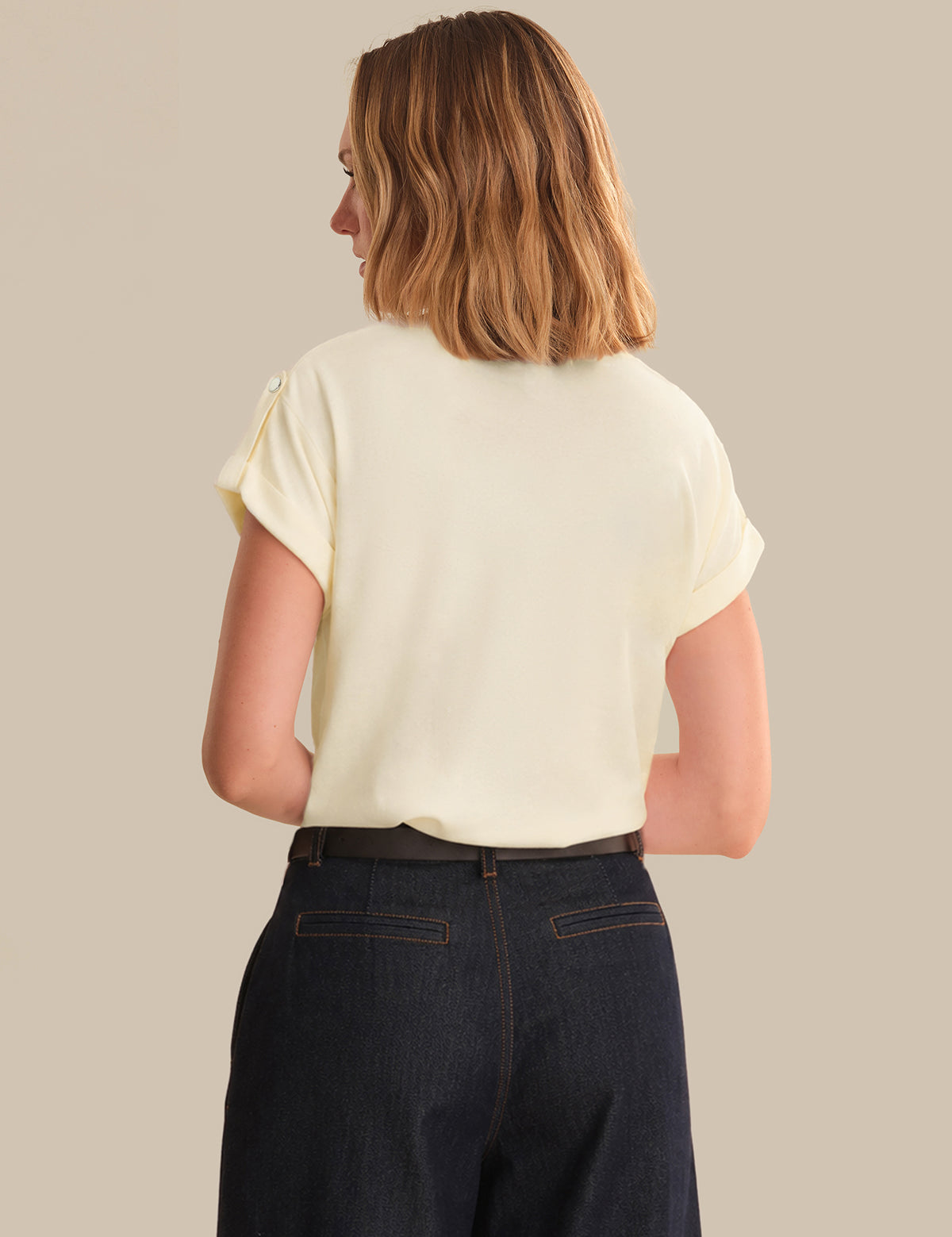 Person wearing a light-colored top and dark jeans on a beige background