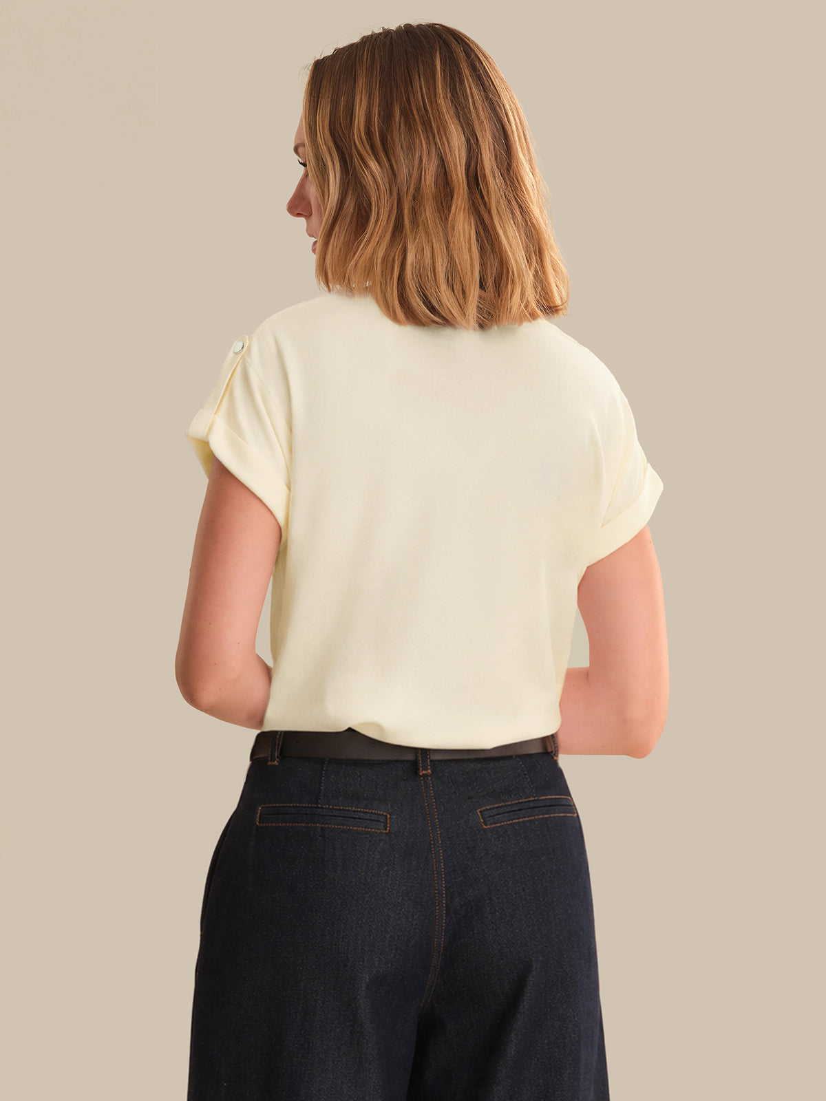 Person wearing a light-colored top and dark jeans on a beige background
