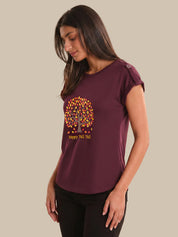 Woman wearing a maroon t-shirt with a colorful tree design and text on a beige background