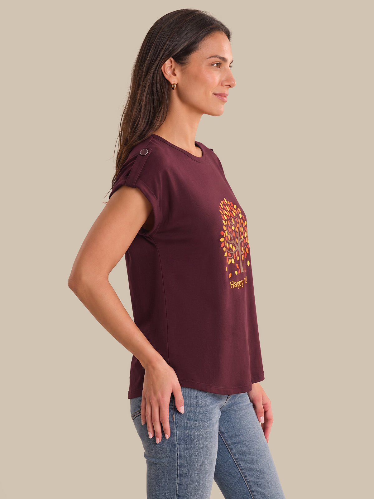 A woman wearing a short-sleeve maroon t-shirt with a colorful graphic on the front, paired with light blue jeans, shown in profile against a solid beige background.