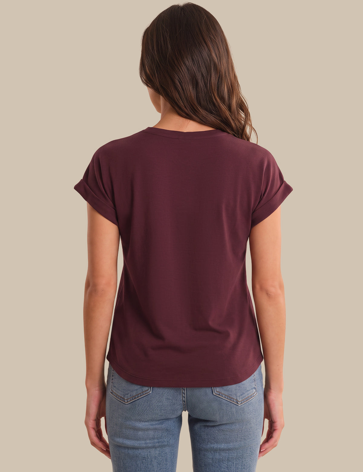 A woman viewed from the back wearing a short-sleeve crew-neck t-shirt in maroon and light-wash blue jeans, set against a solid beige background.