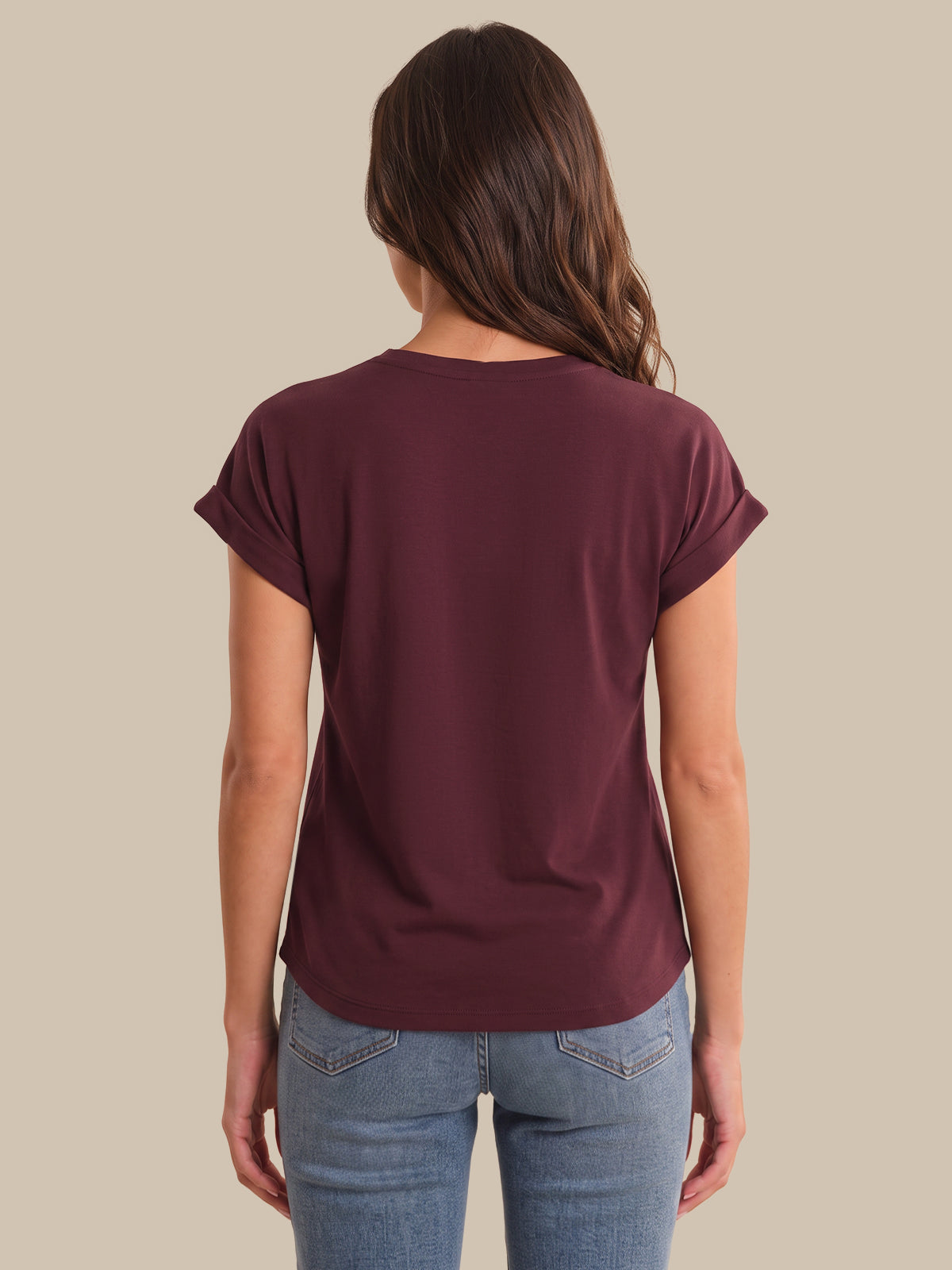 A woman viewed from the back wearing a short-sleeve crew-neck t-shirt in maroon and light-wash blue jeans, set against a solid beige background.