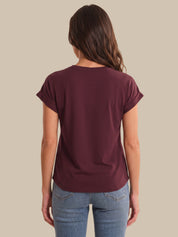 A woman viewed from the back wearing a short-sleeve crew-neck t-shirt in maroon and light-wash blue jeans, set against a solid beige background.