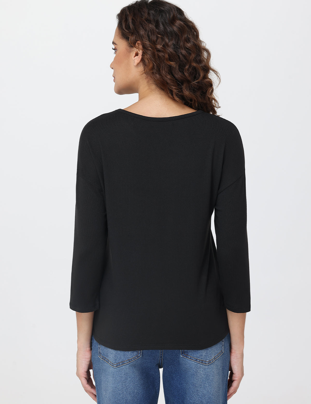 Woman wearing a black top and blue jeans on a light gray background