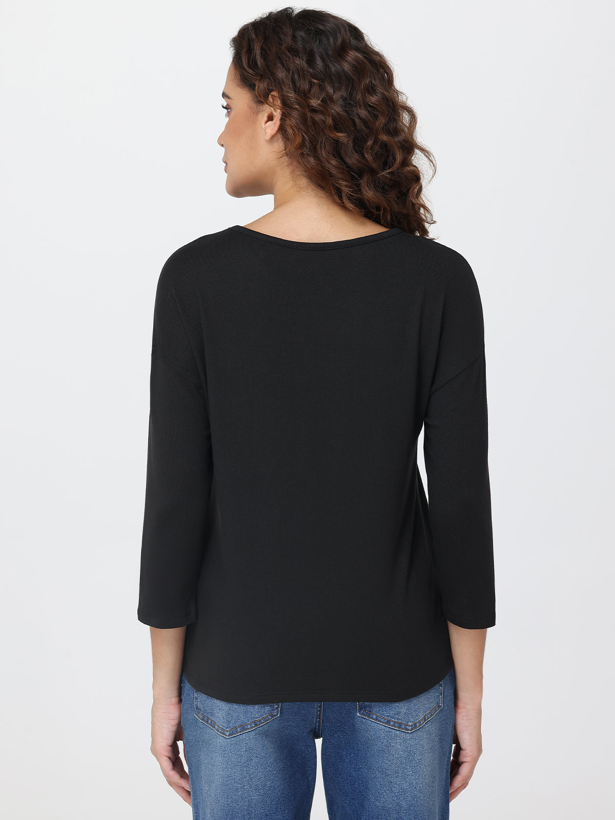 Woman wearing a black top and blue jeans on a light gray background