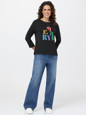Woman wearing a black top with colorful text and blue jeans on a white background