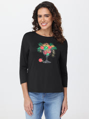 Woman wearing a black long-sleeve shirt with a glass design featuring fruits and flowers on a white background.