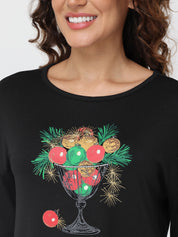 Black top with a festive design of Christmas ornaments and greenery on a plain background.