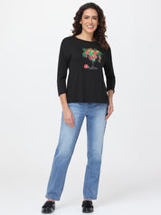Woman wearing a black top with a floral and dog illustration and blue jeans on a white background