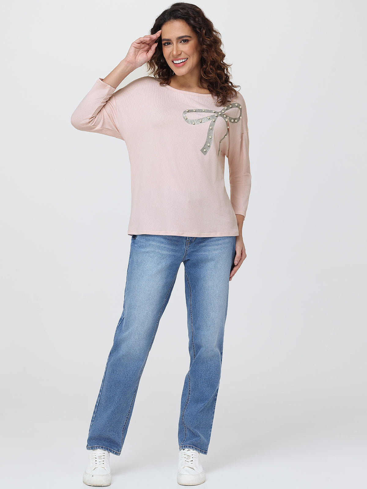 Woman wearing a light pink top with a decorative element and blue jeans on a white background