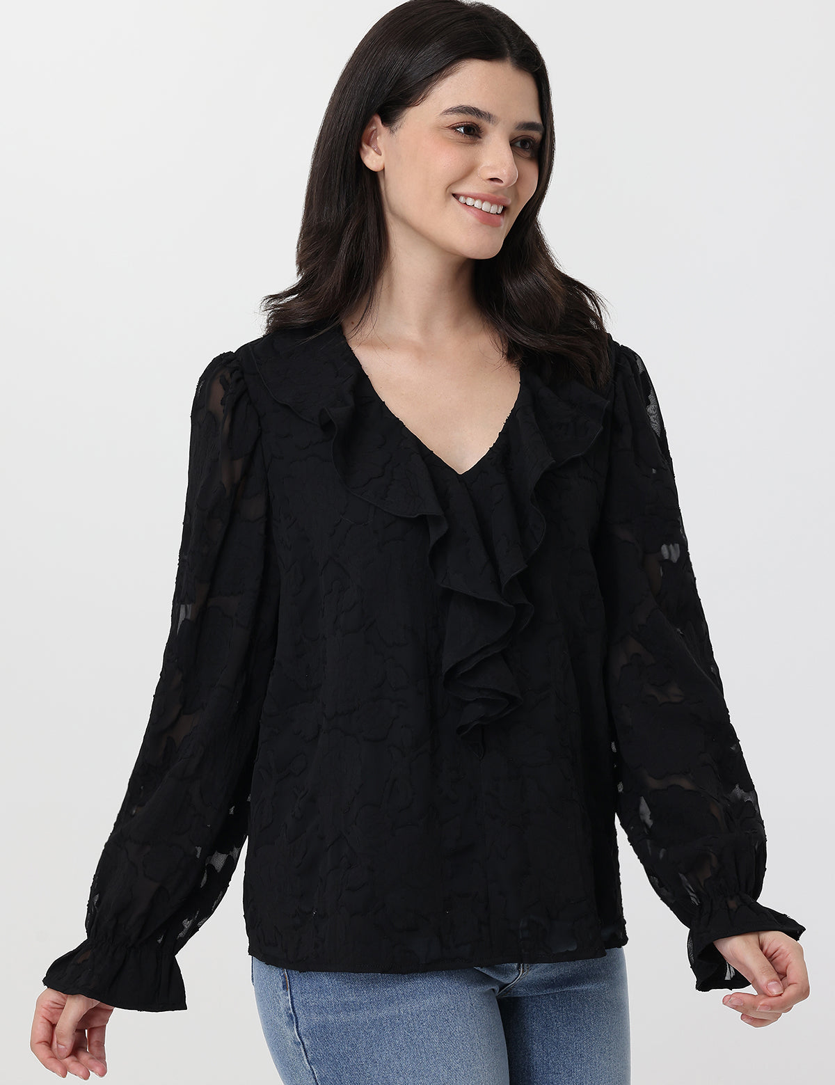 Woman wearing a black ruffled blouse with blue jeans on a white background
