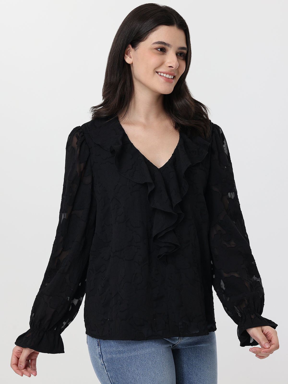 Woman wearing a black ruffled blouse with blue jeans on a white background