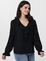 Woman wearing a black ruffled blouse with blue jeans on a white background