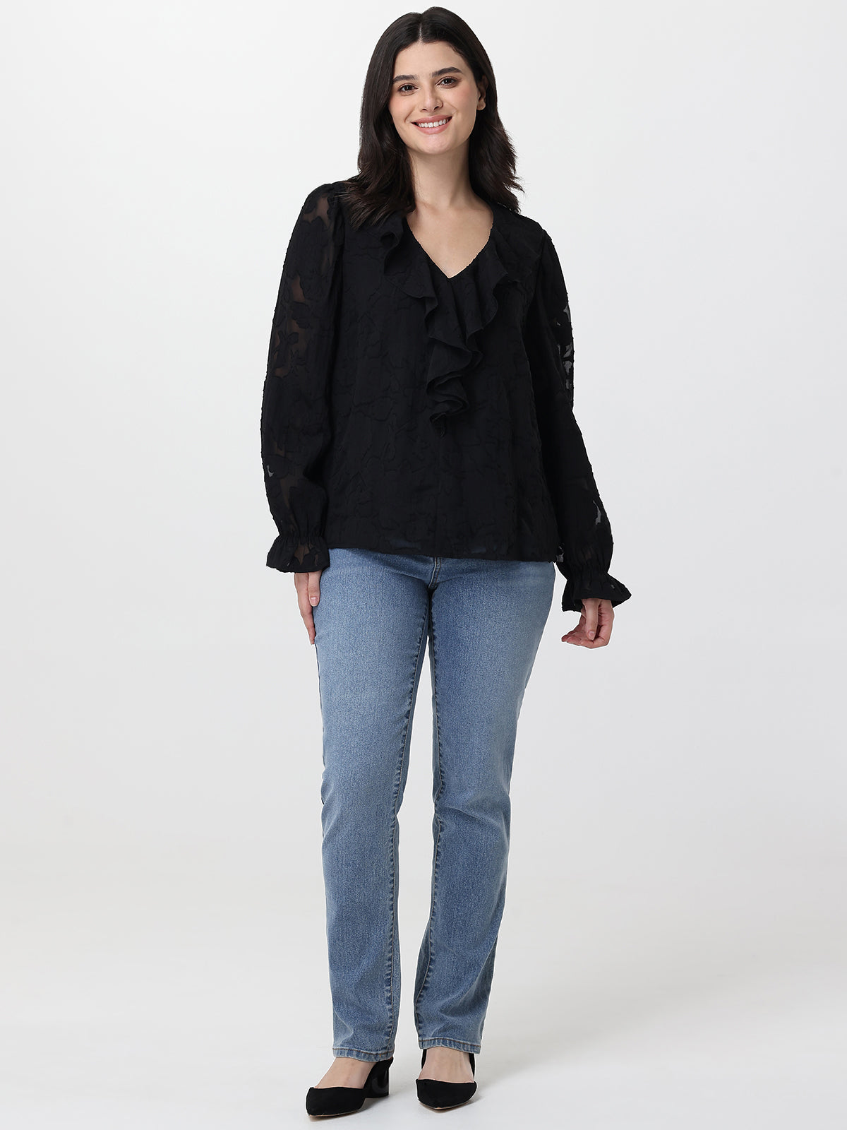Woman wearing a black blouse with ruffles and blue jeans on a white background