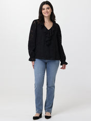 Woman wearing a black blouse with ruffles and blue jeans on a white background
