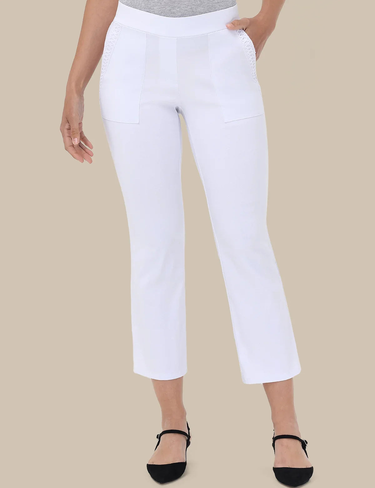 White cropped pants with decorative stitching on the front pockets, shown on a model wearing a gray top and black flat shoes against a solid beige background.