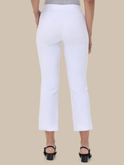 White cropped ankle-length pants shown from the back on a model, paired with black heeled sandals against a solid beige background.