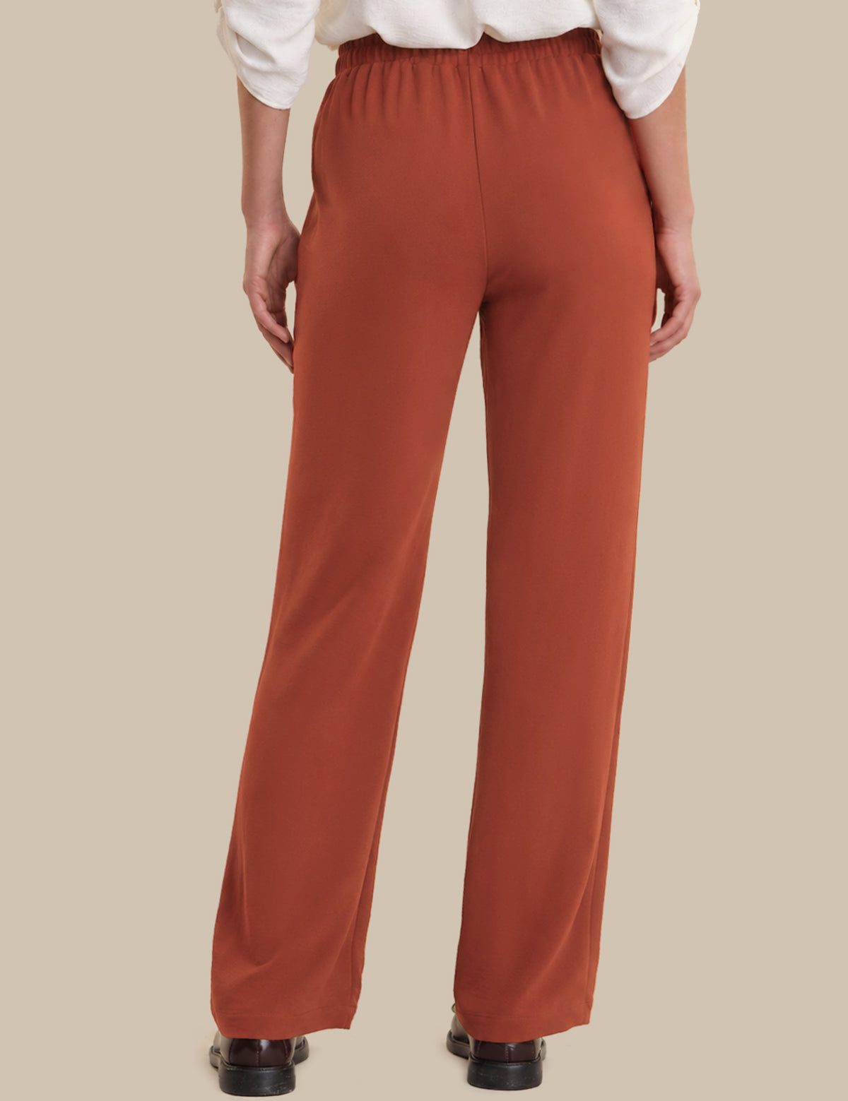 Person wearing rust-colored pants on a beige background