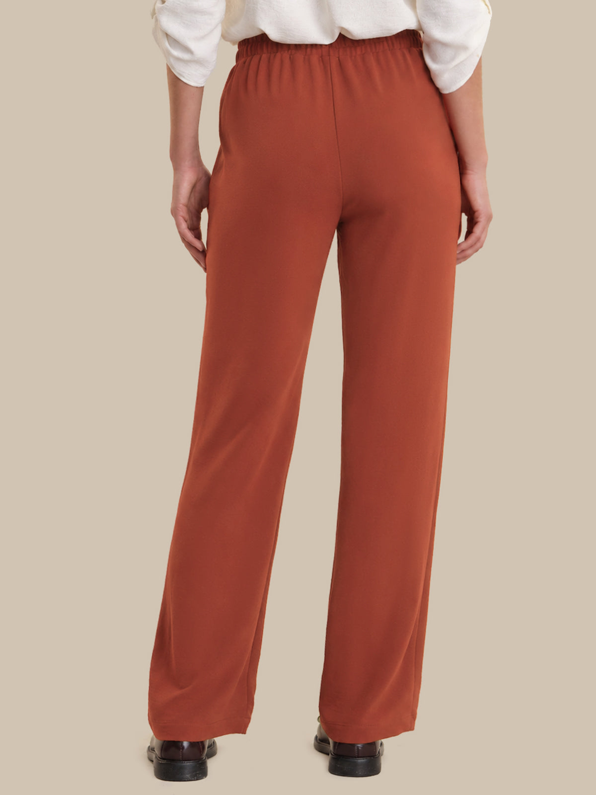 Person wearing rust-colored pants on a beige background