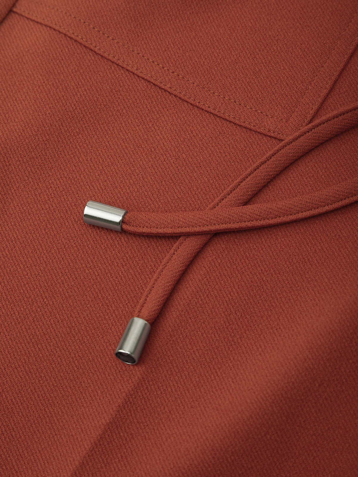 Close-up of a rust-colored hood with drawstrings on a matching fabric background