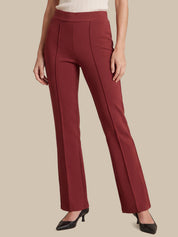 A model wearing a pair of high-waisted, straight-leg trousers in a deep burgundy red, paired with a cream ribbed top and black pointed-toe heels, set against a solid beige background.
