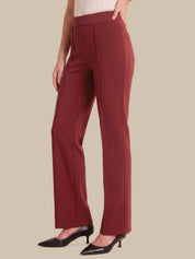 A model wearing a pair of high-waisted, wide-leg trousers in a deep burgundy red, paired with black pointed-toe pumps, shown against a solid beige background.