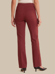 A person shown from the back wearing straight-leg trousers in a deep burgundy red, paired with a cream ribbed top and black pointed-toe heels, against a solid beige background.