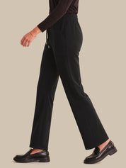 Person wearing black pants and black shoes on a beige background