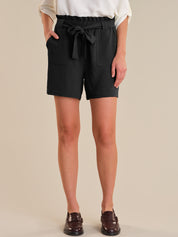 Person wearing black shorts with a tie waist on a beige background