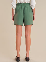 Person wearing green shorts and a white shirt on a beige background