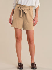 Person wearing beige shorts with a tie waist on a plain background