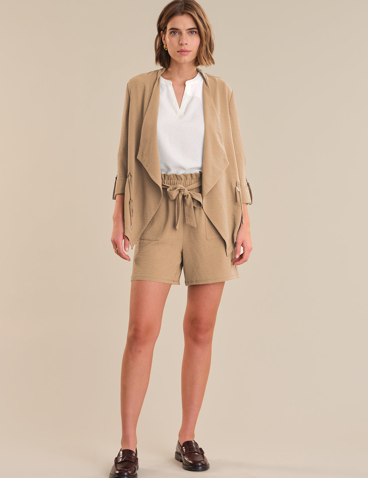 Woman wearing a beige outfit with a jacket and shorts on a beige background