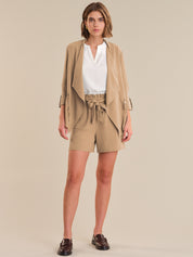 Woman wearing a beige outfit with a jacket and shorts on a beige background