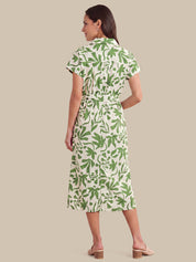 A woman shown from the back wearing a short-sleeve midi dress with a green leaf pattern on a cream background, paired with beige block-heel mule sandals, against a solid beige studio background.