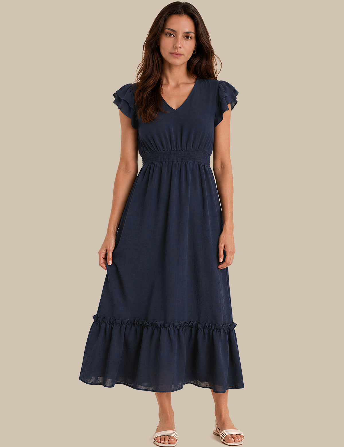 A woman modeling a navy blue midi dress with ruffled cap sleeves, a V-neckline, a gathered waist, and a tiered ruffle hem, set against a solid beige background.